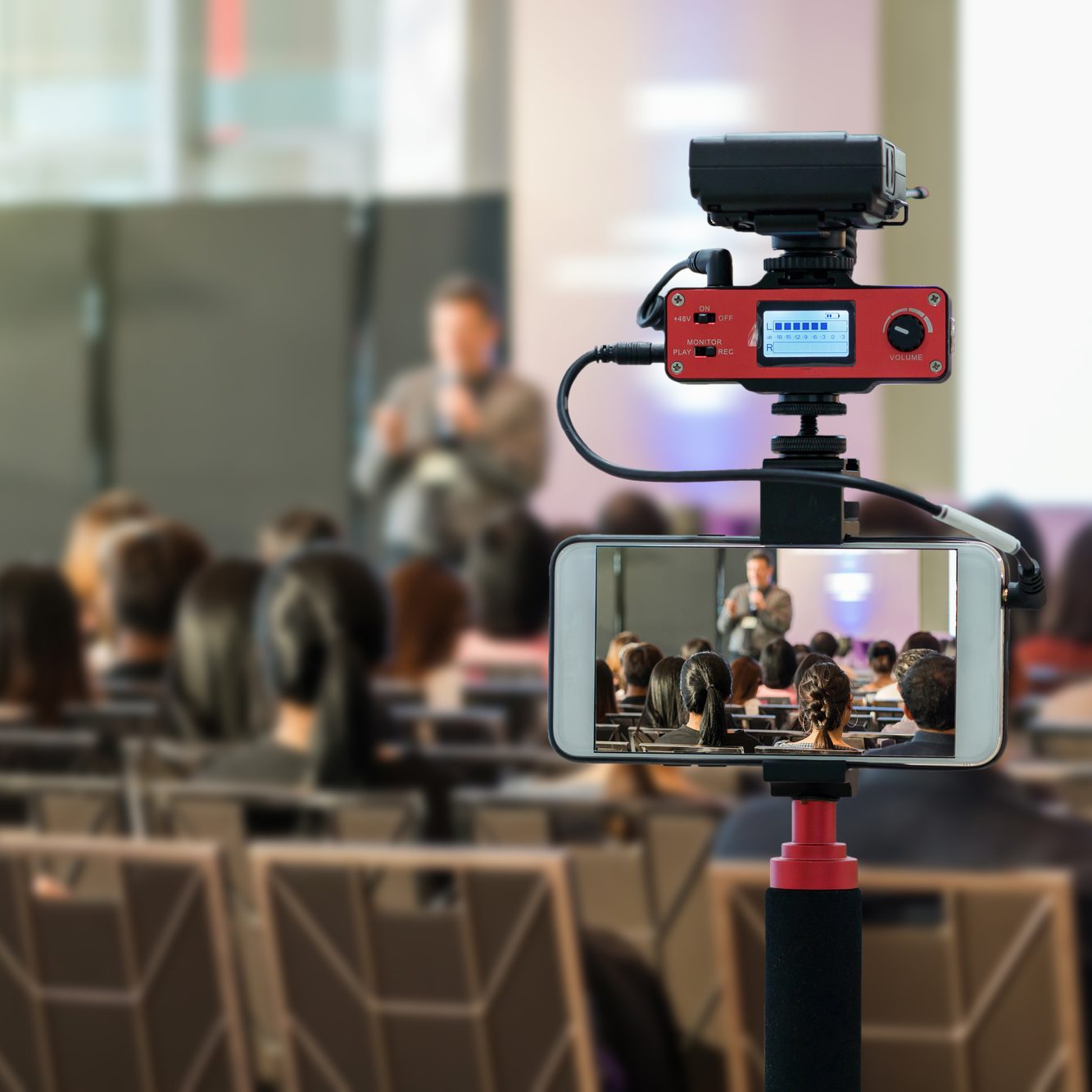 Closeup smart mobile phone taking Live over Speakers on the stage with Rear view of Audience in the conference hall or seminar meeting, technology live streaming and broadcast concept